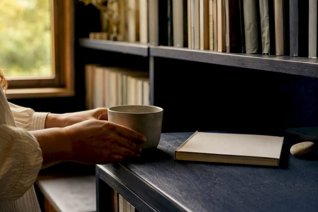 Hands placing cup on table next to phone and stone
